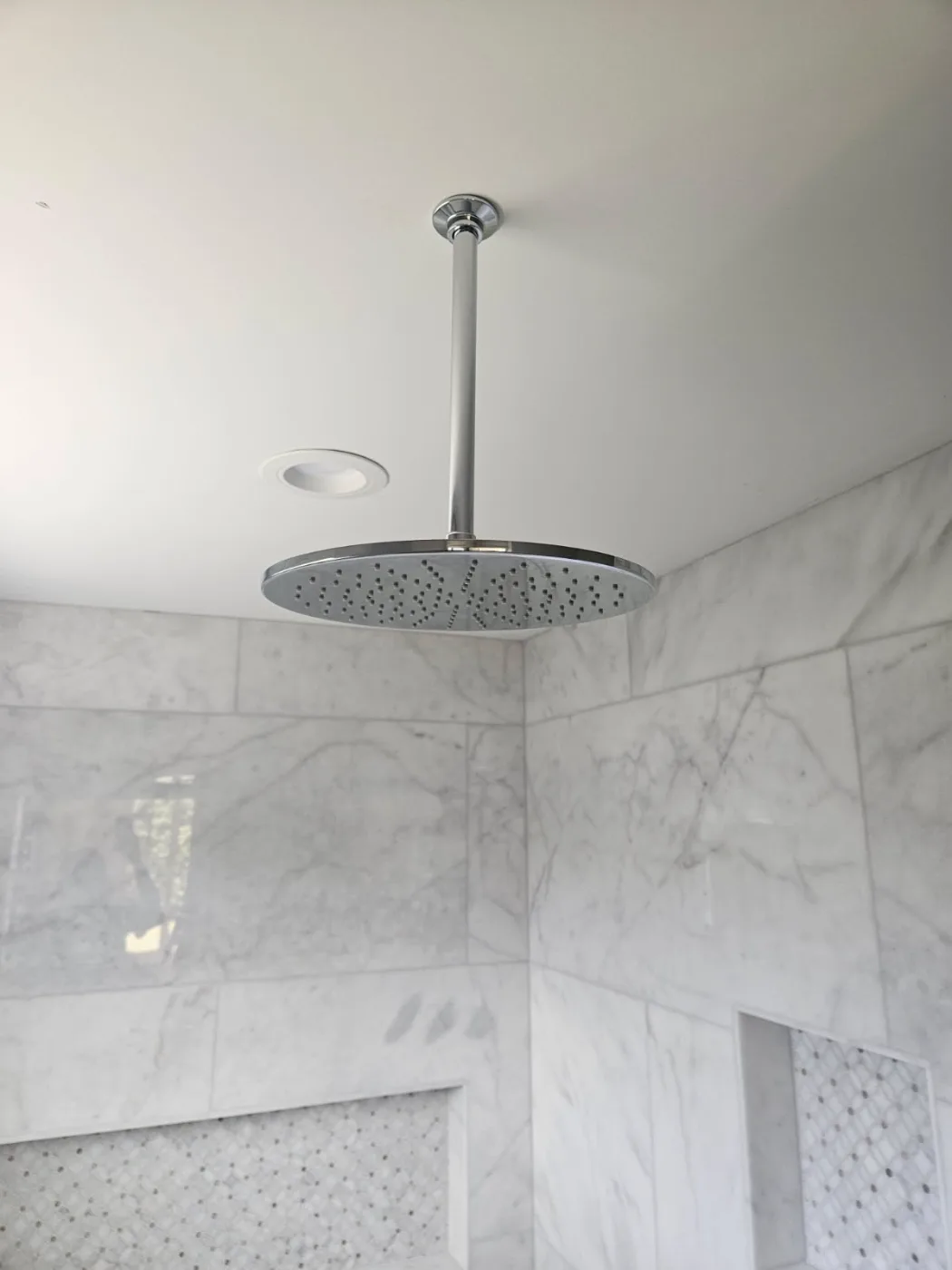 Ceiling-mounted chrome rain shower head installed in a marble shower